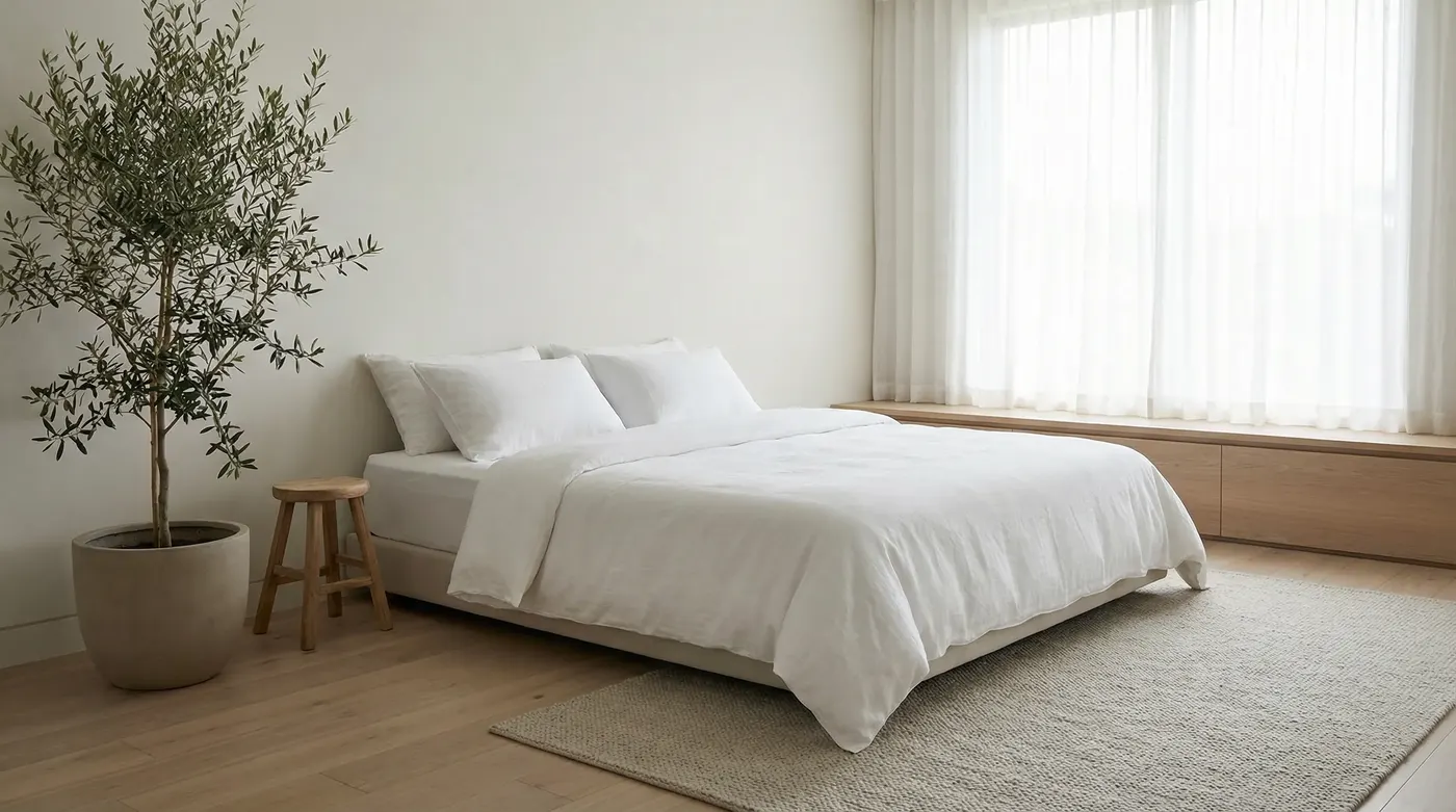 Clean, minimal bedroom interior with light timber flooring and white bedlinen — calm, wellness-focused lifestyle photography, natural light